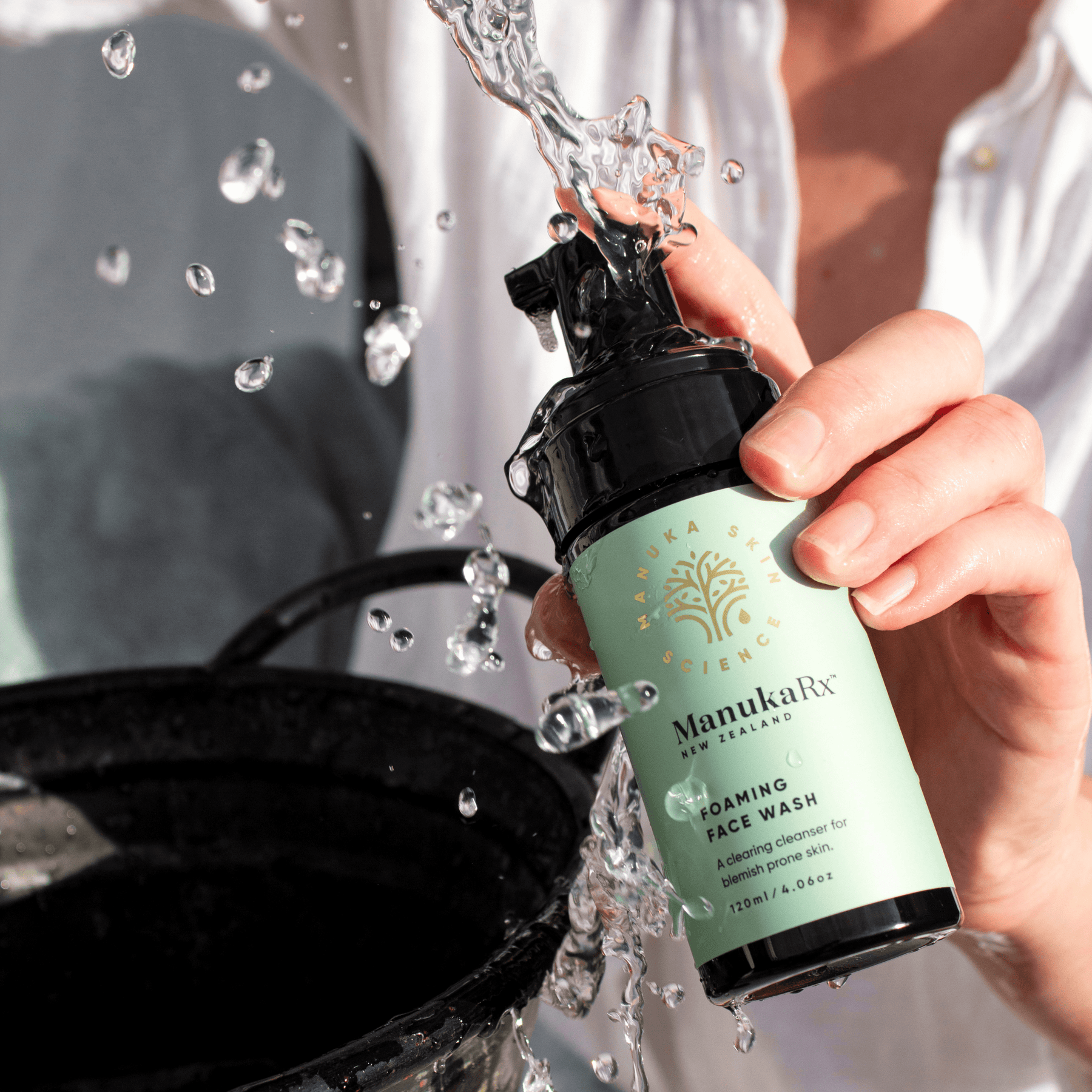 Woman holding bottle of ManukaRX Foaming Face Wash with water splashing onto the bottle